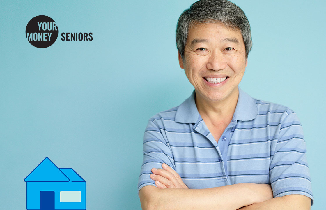 senior man with arms crossed standing beside a small house icon and a logo that says your money seniors